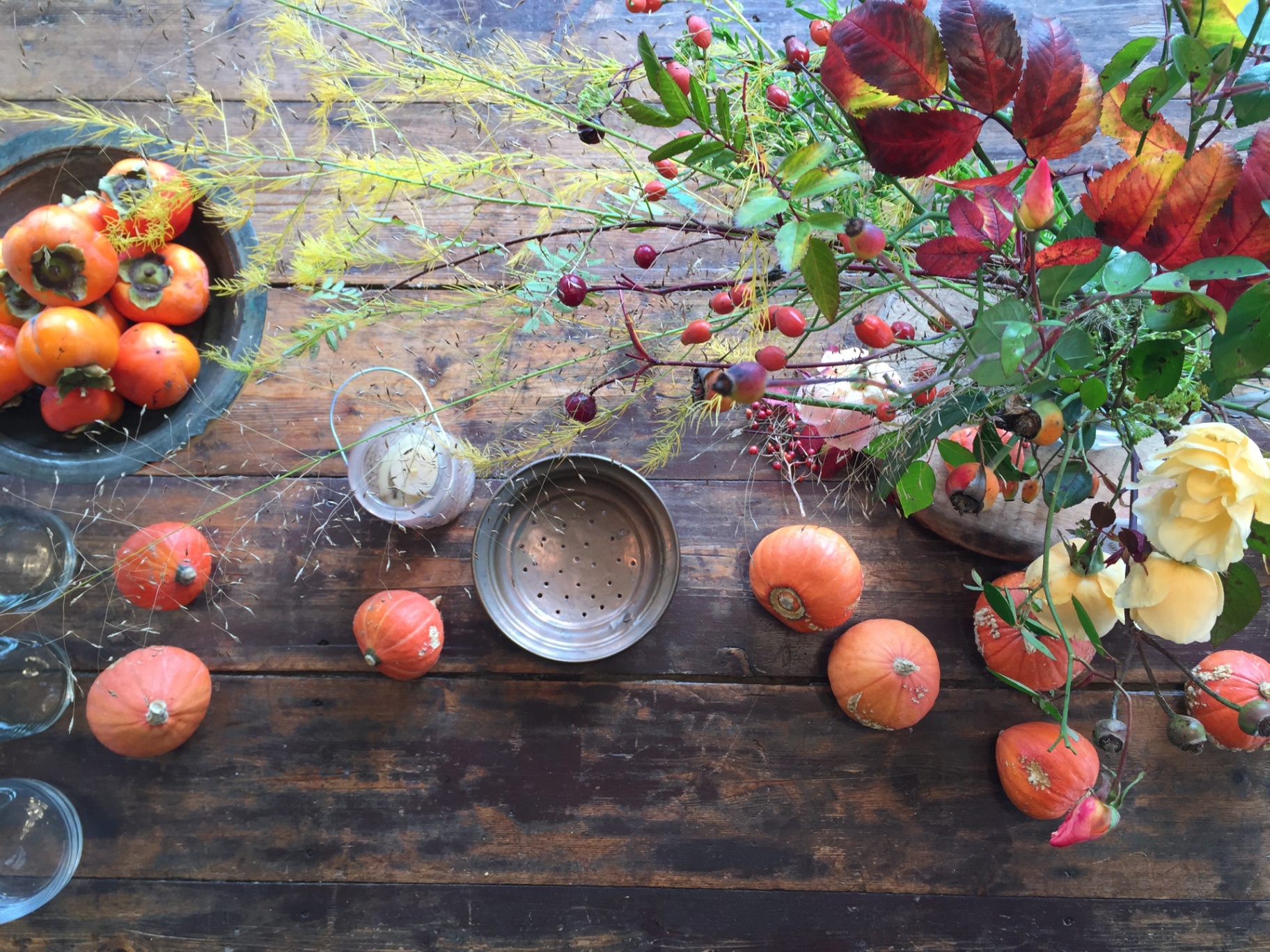 Autumn still life with persimmons, pumpkins, roses and rose hips on a weathered wooden table